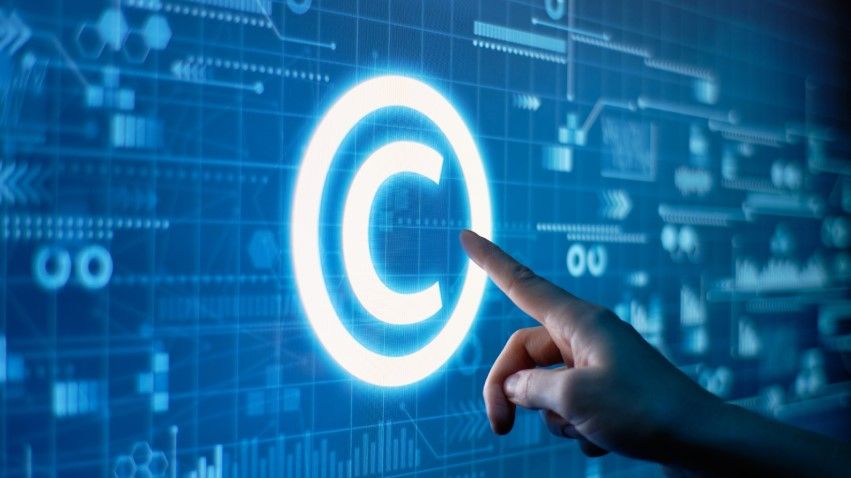A hand points toward a glowing copyright symbol on a digital blue background, emphasizing protecting code for software developers amid various technological and data graphics.